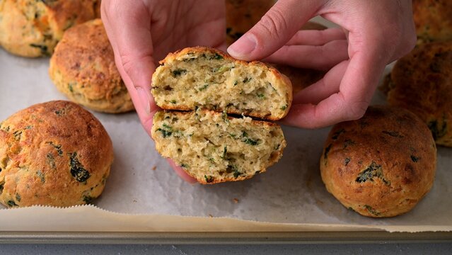 Fresh homemade spinach and parmesan savory biscuit broken in half by hands, showing soft fluffy inside texture. Golden baked cheese and spinach biscuit, perfect savory snack for breakfast, brunch, or