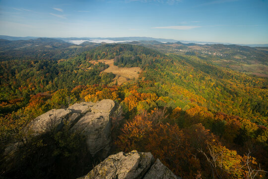 Aerial view of Tatarska luka surrounded by autumn forests with vibrant foliage, rocky outcrops in the foreground, and distant hills in Ilija, Banska Bystrica Regio, Slovakia.
