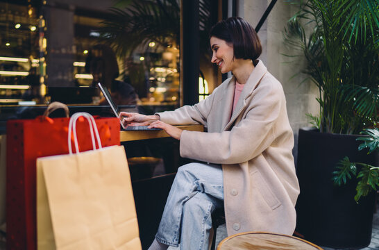 Smiling woman typing on tablet keyboard sitting at outdoor cafe, female professional working remotely on 5G device after shopping, lady entrepreneur using mobile office technology in city, profile.