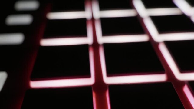 Close-up of MIDI controller grid with illuminated pads changing colors in the dark. Concept of electronic music production, nightlife technology, and modern DJ equipment.