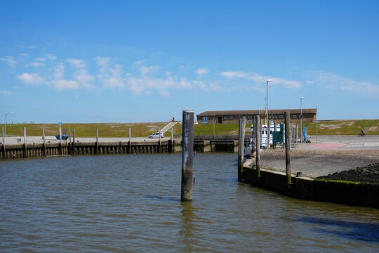 A scenic view of a part of the Schl&uuml;ttsiel harbor basin in North Friesland, Germany, looking towards the mainland with traditional wooden poles in the water and a ship hidden in the background