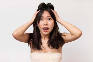 Fototapeta premium Stressed Young Asian Woman With Hands On Head Expressing Shock And Overwhelm In A Neutral Setting. Displaying Emotion Of Concern And Anxiety, Reflecting Modern Lifestyle Challenges.