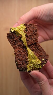 Dubai style chocolate muffin cut in half with pistachio paste and kataifi filling held in female hand. Dessert food photography. Bakery pastry and sweet snack concept. Close-u,p selective focus shot.