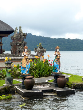 Colorful Balinese goddess statues with clay pots and flowers at Ulun Danu Beratan Temple garden, Bedugul, Bali, with temple shrines.