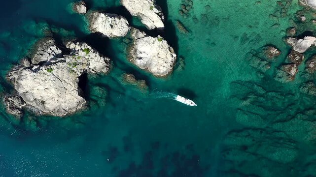 Aerial view of a sightseeing boat cruising beneath the spectacular cliffs of Tossa de Mar, navigating crystal-clear waters beside rocky reefs and secluded coves. 