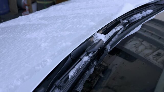 Frozen car windshield wiper blade rests against the glass covered in thick winter snow and ice. This concept illustrates vehicle maintenance difficulties in freezing weather conditions.