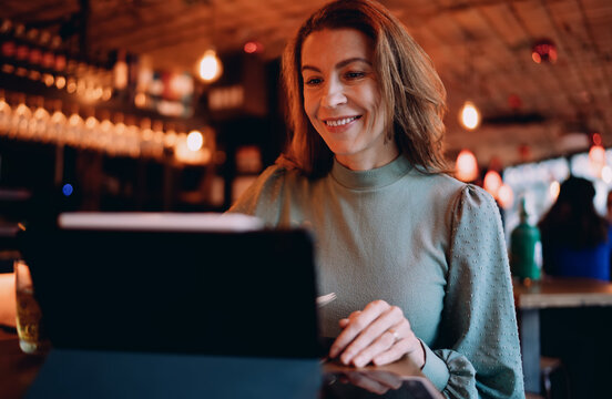 Smiling Caucasian woman using digital tablet at cafe, female professional attending webinar, career growth and online education concept, authentic representation of digital nomad lifestyle.