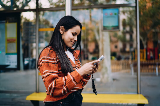 Portrait of smiling mixed race girl with phone on bus stop bench, authentic representation real people inclusion equity diversity, low angle perspective.