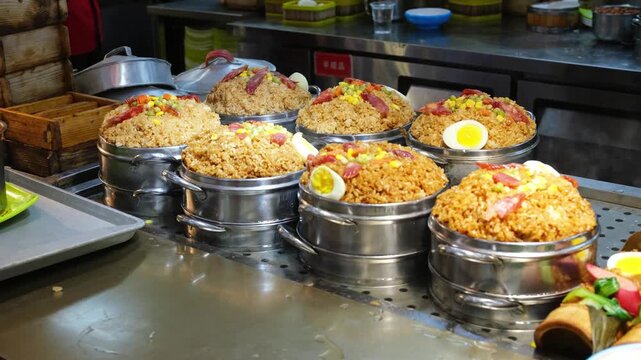 steamed rice with sausage is displayed in metal pot at busy food market. hot rice offers rich flavor for hungry visitors. traditional rice is cooked in large steamer and wrapped in leaf.