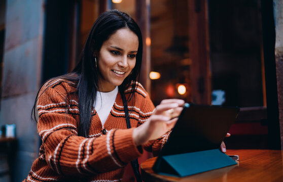 Smiling mixed race woman using tablet computer at street cafe, happy hispanic freelancer working remotely with gadget, digital nomad lifestyle and online communication, authentic representation.