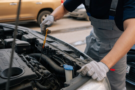 Close-up of mechanic hands in gloves checking car engine oil level with dipstick. Professional auto service and vehicle maintenance. Open hood at repair shop.