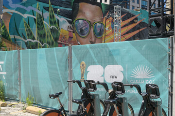 Naklejka premium Bike Share Toronto station at Nelson St / Duncan St with view of FIFA World Cup mesh banner fence and mural (by Clandestino's Art) at RendezViews (Casamigos alcohol)