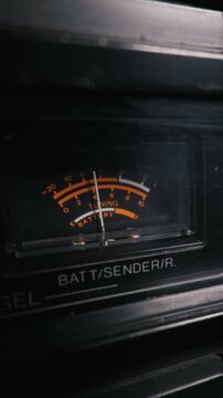 Vintage analog VU meter sits on dark electronic audio equipment. The illuminated tuning dial displays orange and white measurement scales. A white needle indicates the current battery level.