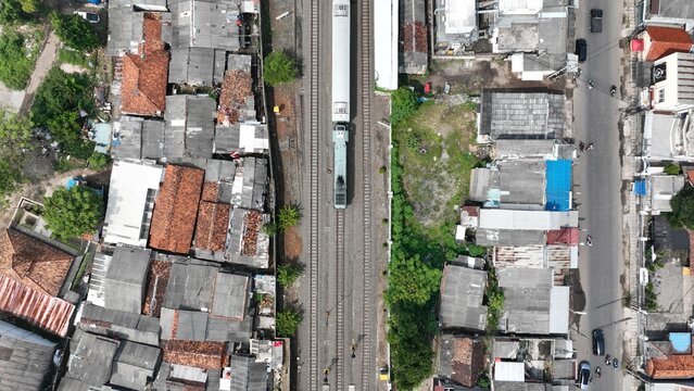 Aerial view of a train traveling on tracks through a densely populated urban neighborhood with terracotta rooftops and narrow streets in Kasemen, Banten, Indonesia.