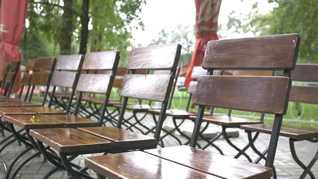 A low-angle, medium shot shows a neat row of empty, polished wooden folding chairs with black metal frames set up for an outdoor event or caf&eacute; seating in a park.