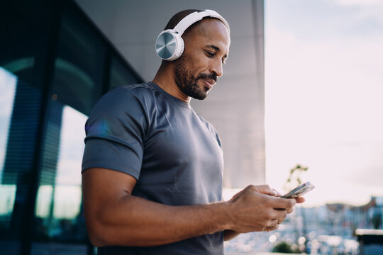 Athletic man browsing on mobile phone outdoors, person using smartphone application on city plaza after training, digital connection and wireless technology, authentic representation, copy space.