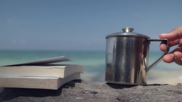 Stack of Books and Stainless Mug on Driftwood by the Sea for Relaxing Beach Reading and Coffee