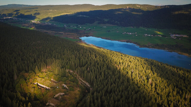 Aerial view of Lac des Rousses surrounded by dense coniferous forests and rolling hills in Les Rousses, Bourgogne-Franche-Comte, France.
