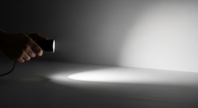 Hand holding a black flashlight shining a bright beam of light. Spotlight on a dark grey surface. Concept of search, discovery, and guidance