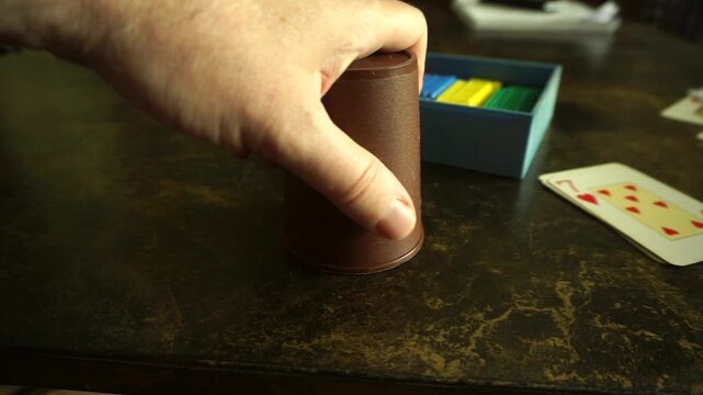 Male hand shaking a leather cup and revealing a winning combination of poker dice on a game table
