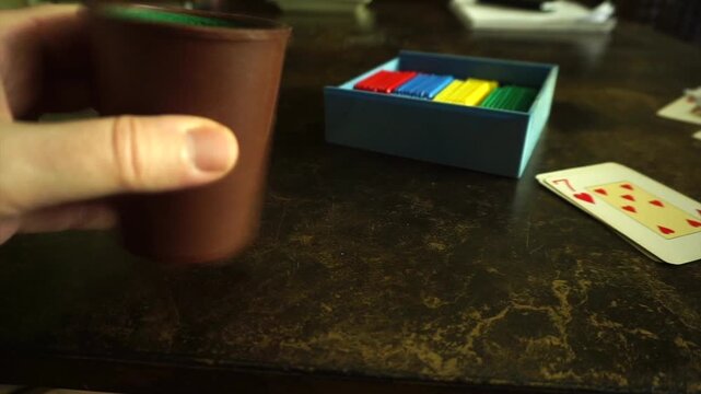 Person's hand shaking a dice cup and rolling poker dice on a table during a gambling game