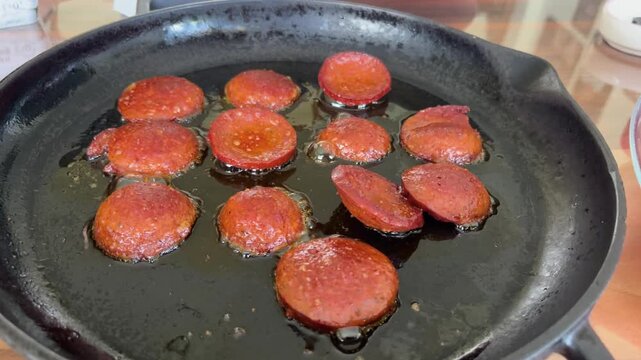 Delicious, juicy slices of sucuk sizzling away in a hot skillet. Enjoy a traditional Turkish breakfast with the crispy sucuk, served straight from the skillet with a fork.