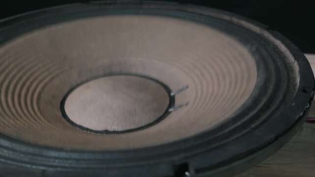 A close-up view of a large black subwoofer cone vibrating intensely while playing loud bass music. Concept of audio power, low frequency sound waves, and musical vibration technology.