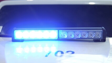 Blue Police Light Flashing Atop Patrol Car Hood Showing Illuminated Decal, Intense LED Glow Reflecting On Wet Surface, Highcontrast Night Mood, Urgent Response Vibe, Public Safety Signal. © bisonov