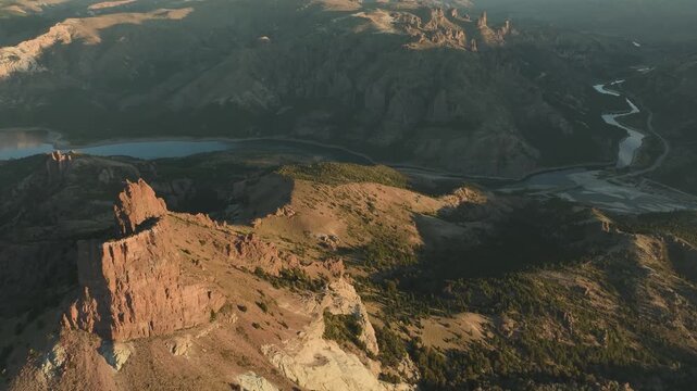 Aerial view of rugged rock formations, mountain ridges, and the river confluence of Valle Encantado, Patagonia, Argentina, illuminated by golden sunset light.