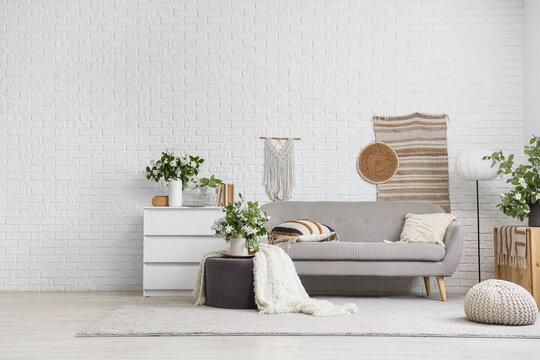 Modern living room interior with gray sofa, white brick wall, and bohemian decor elements
