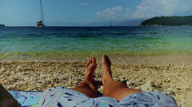 Tourist Sunbathing On Pebble Beach Looking At Turquoise Sea Waves.  Relaxation On Shore Near Yacht