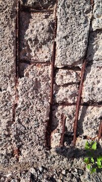 Slow motion detail of a damaged reinforced concrete wall with crumbling cement and exposed rusted rebar, showing signs of decay and structural problems due to spalling and corrosion