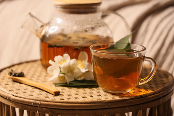 Obraz premium Relaxing jasmine tea moment with glass teapot and cup on woven tray, cozy home comfort and wellness beverage, fresh jasmine flowers and a wooden spoon with tea leaves complete the tranquil composition