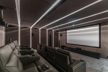 Six leather chairs are arranged in front of a large white screen in a home theater. Lights create a bright effect on the walls. A projector is mounted, ready for use © Alhim