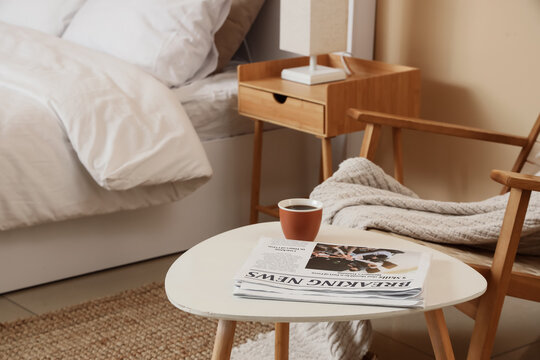 Morning coffee and newspaper on white table in cozy bedroom with bed and wooden furniture, the scene includes a comfortable bed with white linens and wooden furniture