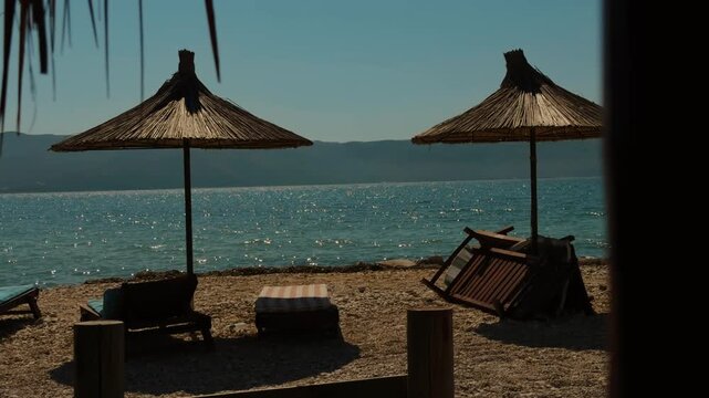Two Straw Umbrellas And Lounge Chairs On Empty Pebble Beach. Relaxing Tropical Resort Coast Landscape