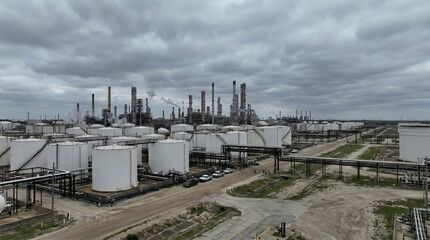 Obraz premium Wide view of industrial oil refinery with storage tanks and processing towers under cloudy sky