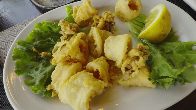 Fried Calamari Rings On Green Lettuce Leaves With Lemon Slice. Crispy Golden Battered Squid. Mediterranean Cuisine