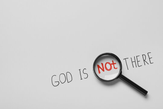Magnifying glass "not" in "god is not there" text on white background, atheism and doubt