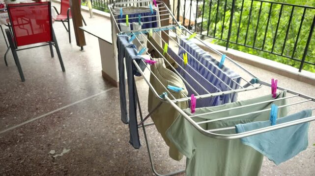Wet Clothes Hanging On Drying Rack With Colorful Plastic Clothespins On Outdoor Balcony. Housework Laundry