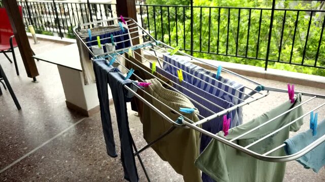 Wet Clothes Hanging On Metal Drying Rack With Colorful Clothespins. Laundry Drying On Balcony