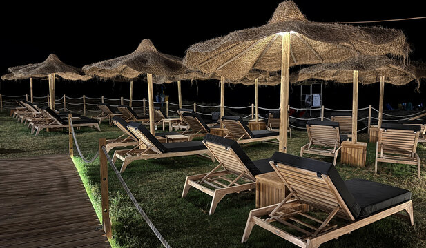 Luxury Beach Resort at Night with Wooden Sun Loungers and Thatched Parasols