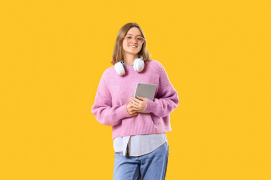 Happy female programmer with tablet and headphones on yellow background