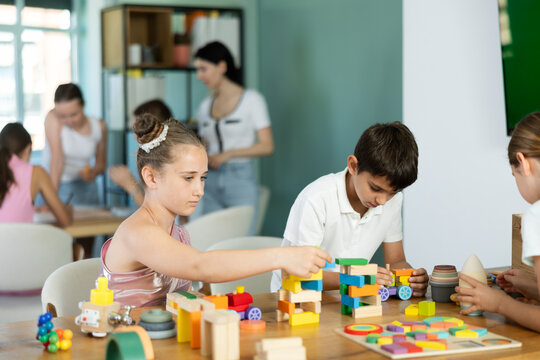 In childrens leisure club, preteens play at table, they stack pyramids, solve puzzles, construct, play with wooden cubes. Summer vacation activity, vacation leisure