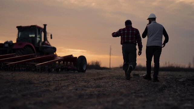 Agribusiness and agriculture, two farmers discussing harvest, walking in fields. Professional agronomist and farmer examining farmland and agricultural machinery, simple rural life in countryside