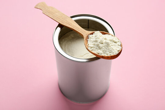 Container of powdered milk with wooden spoon on pink background