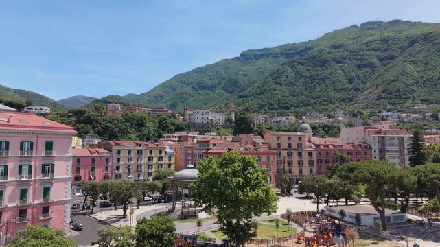 Aerial drone view of Castellammare di Stabia with Villa Comunale park, Cassa Armonica and colorful buildings against lush green mountains, Italy

