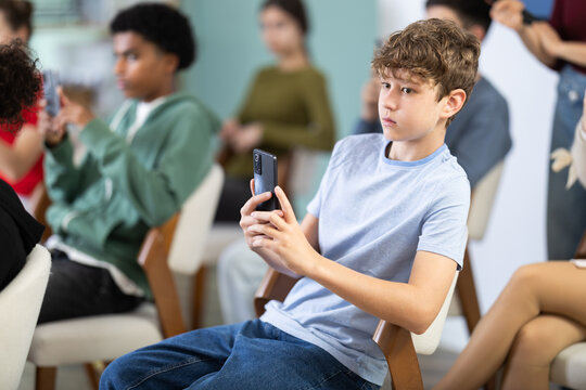 Attentive teenage boy using smartphone to scan QR codes during lesson with teacher in background