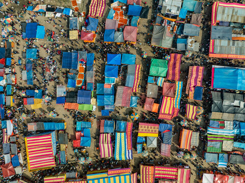Aerial view of a bustling open-air market with colorful fabric stalls, crowded pathways, and shoppers navigating the vibrant marketplace in Bogura, Rajshahi Division, Bangladesh.