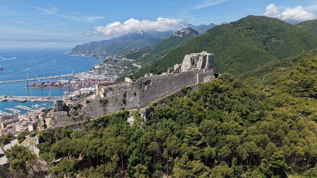 Aerial view of Castello di Arechi long defensive walls stretching across forested ridge above Salerno port, container terminal, and Amalfi Coast mountains, Italy